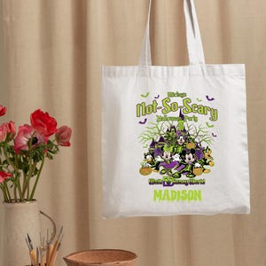 May include: White tote bag featuring a Halloween design with Mickey Mouse, Minnie Mouse, and Donald Duck. The text reads "Mickey's Not-So-Scary Halloween Party" and "Madison".