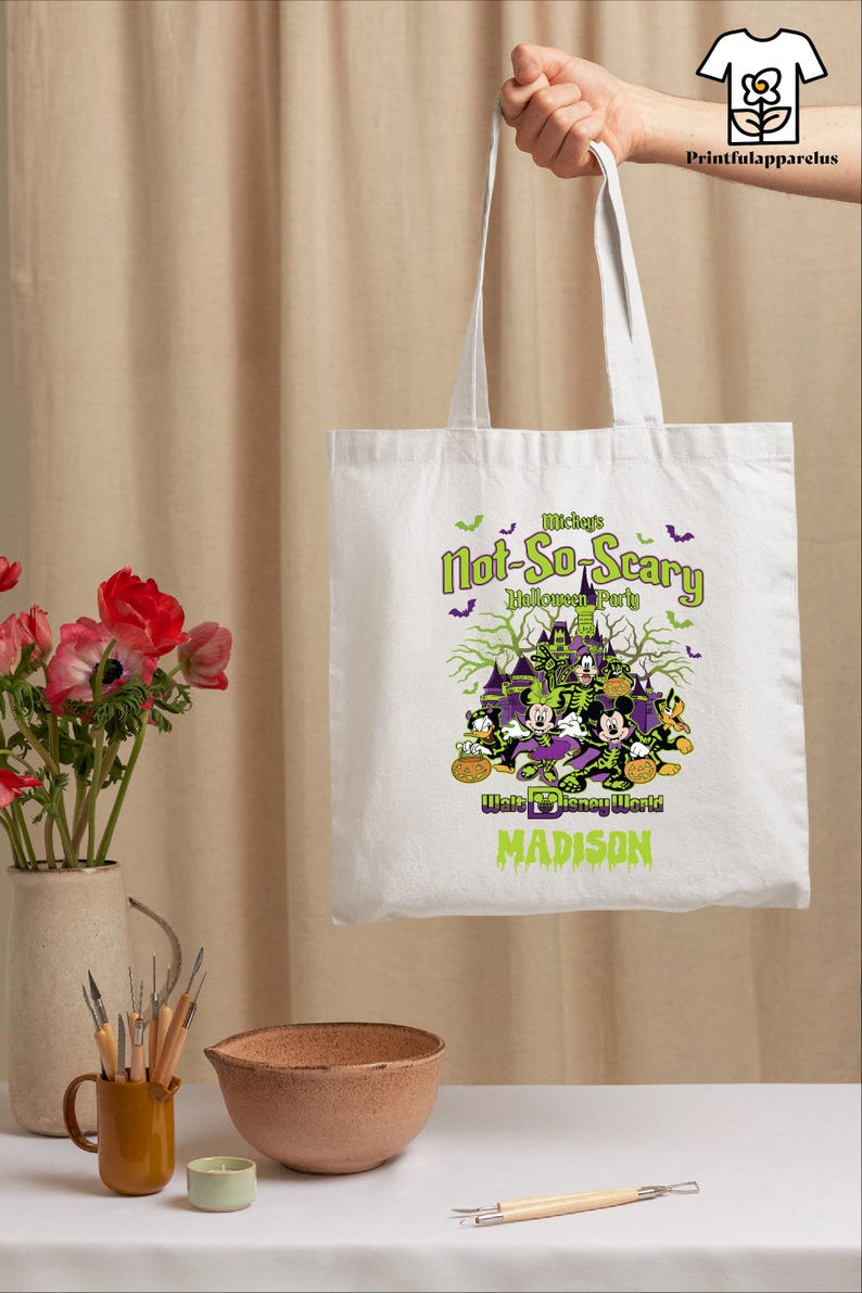 May include: White tote bag featuring a Halloween design with Mickey Mouse, Minnie Mouse, and Donald Duck. The text reads "Mickey's Not-So-Scary Halloween Party" and "Madison".