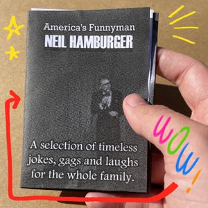 May include: A black and white booklet titled "America's Funnyman NEIL HAMBURGER" held in a hand. The cover features a photo of a man and the text "A selection of timeless jokes, gags and laughs for the whole family."
