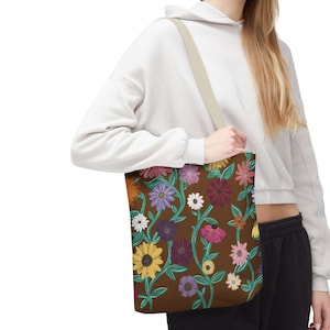 Puede incluir: Un bolso tote marrón con un estampado floral con varias flores coloridas y vides verdes. El bolso tiene una correa beige.