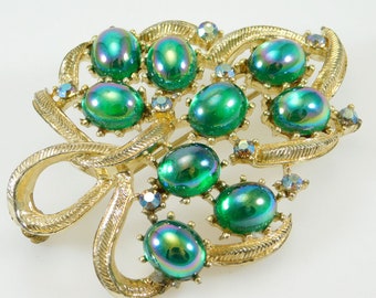 May include: A gold tone brooch with a cluster of iridescent green stones set in a leaf design.