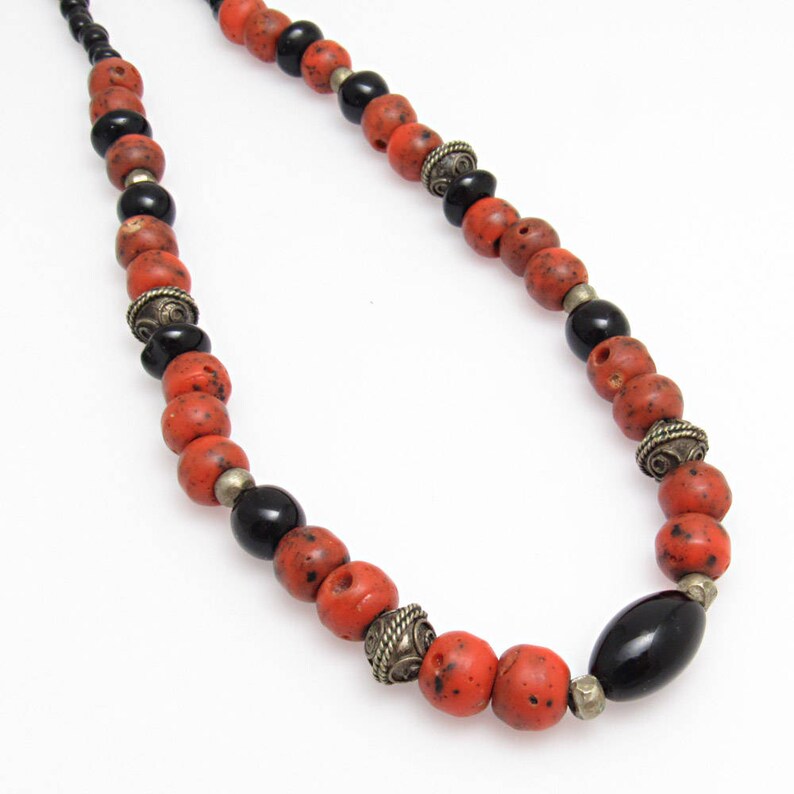 May include: A necklace with red, black, and silver beads. The beads vary in shape, with round and oval designs. The red beads are speckled, while the black beads are smooth and glossy. The necklace is a striking piece.