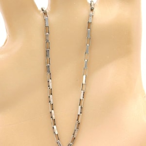 May include: A silver-toned chain necklace featuring a series of rectangular, elongated links connected in a uniform, repeating pattern. The metal has a polished finish, creating a consistent, linear structure that hangs vertically in a simple design.