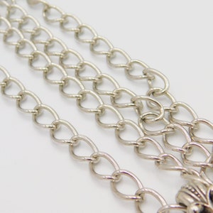 Puede incluir: Un collar de cadena de plata con un cierre decorativo. La cadena est&aacute; hecha de m&uacute;ltiples hebras de metal ovalado enlazado.
