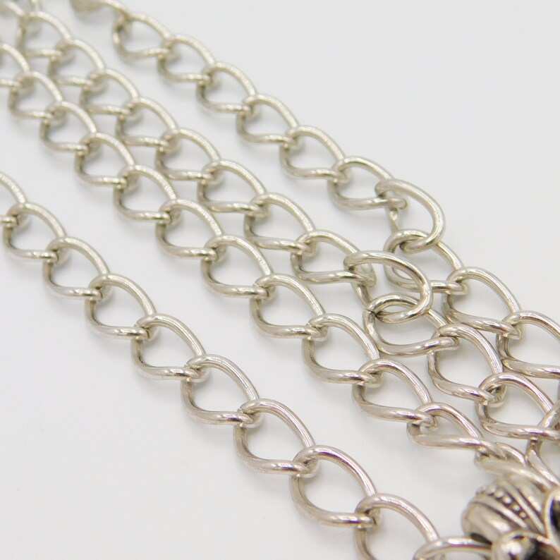 Puede incluir: Un collar de cadena de plata con un cierre decorativo. La cadena est&aacute; hecha de m&uacute;ltiples hebras de metal ovalado enlazado.