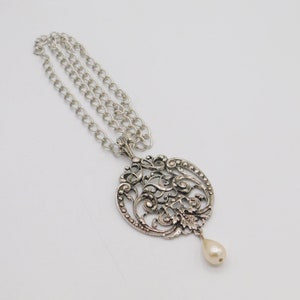Puede incluir: Un collar de plata con un delicado colgante adornado con una perla. El colgante es de dise&ntilde;o circular con un intrincado trabajo de filigrana.