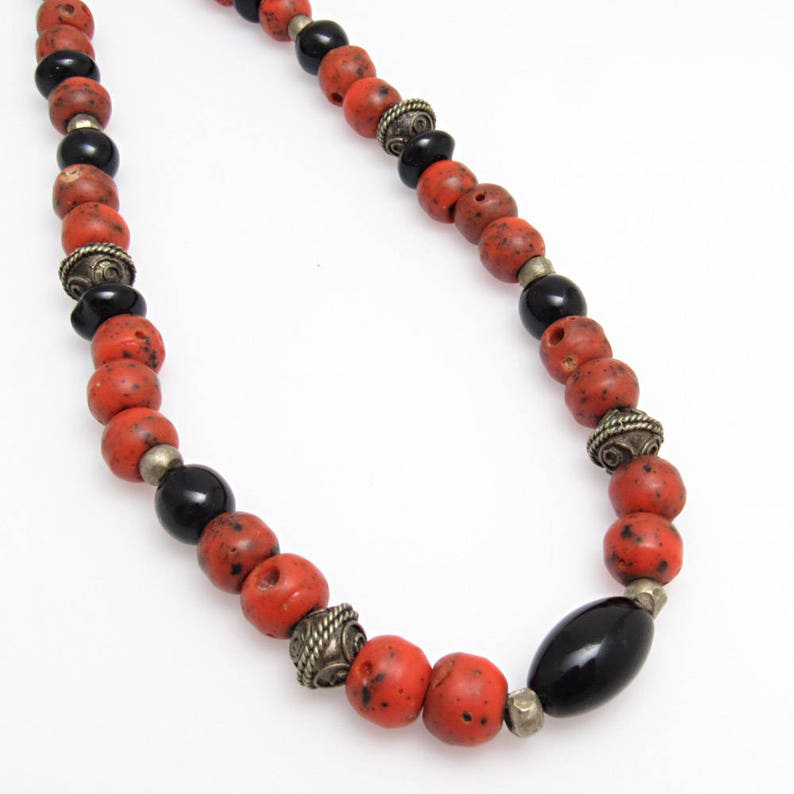 May include: A necklace with red, black, and silver beads. The red beads are speckled, the black ones smooth. Silver-toned metal accents and clasps are incorporated. The necklace is a striking piece of jewellery.