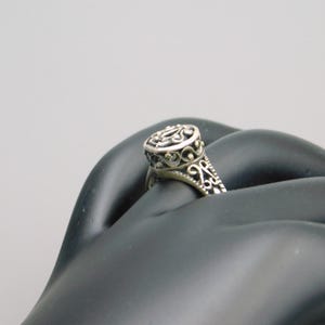Pu&ograve; includere: Un anello in argento caratterizzato da una testa di forma ovale con intricati dettagli in filigrana traforata. Anche la fascia dell'anello presenta motivi decorativi in metallo abbinati che si estendono lungo i lati, creando un aspetto coerente.