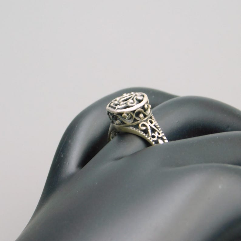 Pu&ograve; includere: Un anello in argento caratterizzato da una testa di forma ovale con intricati dettagli in filigrana traforata. Anche la fascia dell'anello presenta motivi decorativi in metallo abbinati che si estendono lungo i lati, creando un aspetto coerente.