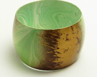 May include: A green and gold bangle bracelet with a marbled design. The bangle is made of wood and has a smooth, polished finish.