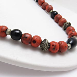 May include: A necklace with a combination of red, black, and silver beads. The red beads have a speckled pattern, and the black beads are smooth and shiny. Silver-coloured spacers and decorative elements provide contrast.
