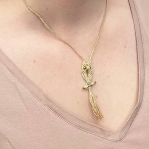 May include: A beige macrame owl necklace with gold beads for eyes and a tassel hanging from the bottom.