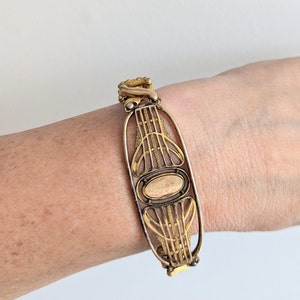 May include: A gold-toned bracelet with an intricate design featuring a central oval shape. The bracelet is made of metal and has a delicate, filigree-like pattern.