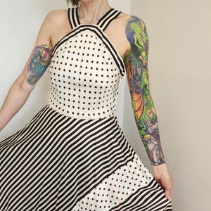 May include: A sleeveless dress featuring a cream-colored bodice with black polka dots and a high halter neckline. The skirt displays a contrasting pattern of diagonal black and white stripes, creating a distinct visual separation between the top and bottom.