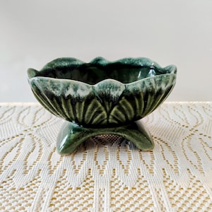 May include: A green ceramic bowl with a scalloped rim and a pedestal base. The bowl has a glossy finish with a dark green color that fades to a lighter green and white near the rim. The bowl is approximately 6 inches in diameter.