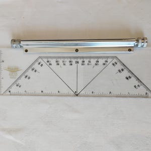 May include: A clear plastic protractor ruler with black markings and a metal guide bar attached to the top edge. The ruler features a central vertical line, angled degree markings from 0 to 170, and imperial inch measurements along the bottom edge.