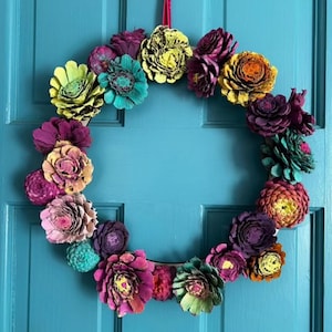 May include: A colorful wreath made of painted pine cones in shades of pink, purple, yellow, and green. The wreath is hanging on a teal door.