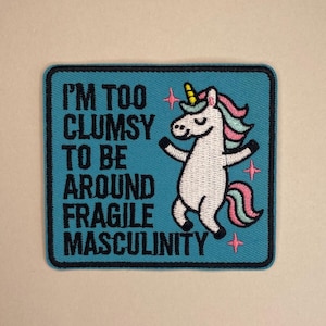 May include: Embroidered patch with a teal background and a black border. The patch features a white unicorn with a rainbow mane and tail, and the text "I'M TOO CLUMSY TO BE AROUND FRAGILE MASCULINITY" in black.