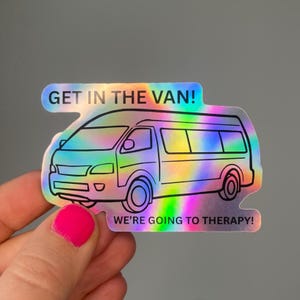 Könnte beinhalten: Holografischer Aufkleber mit einer Van-Illustration und dem Text "GET IN THE VAN! WE'RE GOING TO THERAPY!". Der Aufkleber hat einen Regenbogeneffekt und einen schwarzen Umriss. Der Aufkleber wird von einer Person gehalten.