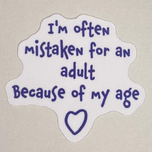 Pode incluir: Um autocolante branco com contorno azul e o texto: "Sou frequentemente confundido com um adulto por causa da minha idade", com um coração azul na parte inferior. O autocolante tem uma forma irregular.