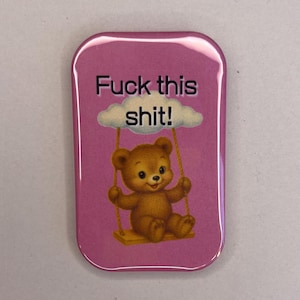 Könnte beinhalten: Ein rechteckiger, rosa Button mit abgerundeten Ecken. Der Button zeigt einen Cartoon-Teddybären auf einer Schaukel unter einer Wolke. Der Text "Fuck this shit!" steht über dem Bären.
