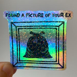 Könnte beinhalten: Holografischer Aufkleber mit dem Text "FOUND A PICTURE OF YOUR EX" über einer schwarzen Müllsack-Illustration. Der Aufkleber hat einen quadratischen Rahmen und einen glitzernden, irisierenden Hintergrund.