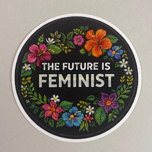 Könnte beinhalten: Runder schwarzer Aufkleber mit dem Text "THE FUTURE IS FEMINIST" in silbernen Buchstaben. Der Text ist von einem farbenfrohen Blumenkranz mit rosa, orangefarbenen, blauen und violetten Blumen und grünen Blättern umgeben.