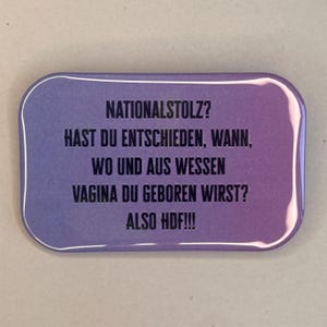May include: A rectangular pin with rounded corners, displaying a purple gradient. The pin has white text that reads "NATIONALSTOLZ? HAST DU ENTSCHIEDEN, WANN, WO UND AUS WESSEN VAGINA DU GEBOREN WIRST? ALSO HDF!!!"