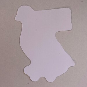 May include: A flat, die-cut sticker in a light cream or off-white color. The shape is irregular, featuring a rounded top section that curves outward to the left and a wider, blocky rectangular extension on the right side, with a wavy bottom edge.
