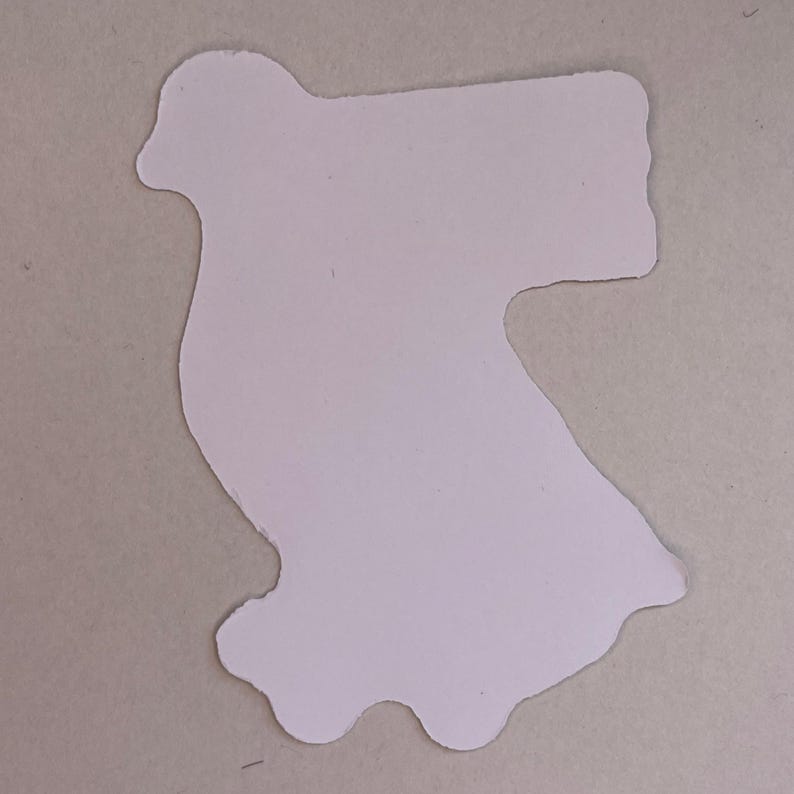 May include: A flat, die-cut sticker in a light cream or off-white color. The shape is irregular, featuring a rounded top section that curves outward to the left and a wider, blocky rectangular extension on the right side, with a wavy bottom edge.
