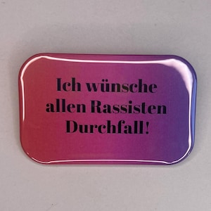 May include: A rectangular button with rounded corners, featuring a gradient background of red and purple. The text "Ich wünsche allen Rassisten Durchfall!" is printed in black.