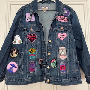 Könnte beinhalten: Eine dunkelblaue Jeansjacke, verziert mit verschiedenen bunten Stickaufnähern, darunter Texte wie Feminist Killjoy, Dump Him, Fries Before Guys, Tears Of My Enemies, Fresh Boys Tears und Male Tears sowie Illustrationen von einer Katze, einem Hasen und einem UFO.