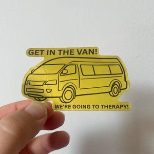 Könnte beinhalten: Ein gelber Aufkleber mit einem Cartoon-Van-Design und schwarzen Umrissen. Der Text "GET IN THE VAN!" steht über dem Van und "WE'RE GOING TO THERAPY!" darunter. Der Aufkleber wird von einer Hand gehalten.