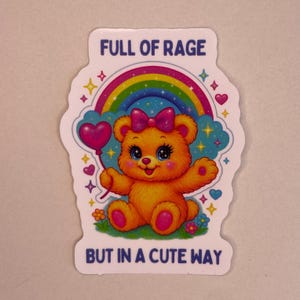 Könnte beinhalten: Ein Aufkleber mit einem Cartoon-Teddybär, einer rosa Schleife und einem herzförmigen Ballon. Der Bär befindet sich vor einem Regenbogen- und Wolkenhintergrund mit dem Text "FULL OF RAGE BUT IN A CUTE WAY".