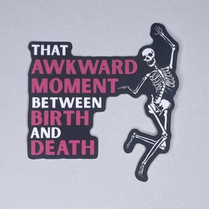 May include: A black sticker featuring the phrase "THAT AWKWARD MOMENT BETWEEN BIRTH AND DEATH" in white and pink. A white skeleton is shown dancing. The sticker has a matte finish and is designed for a humorous effect.