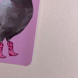 Pode incluir: Um cart&atilde;o retangular com uma ilustra&ccedil;&atilde;o gr&aacute;fica de um pombo cinzento a usar botas de cowboy cor-de-rosa brilhante com padr&otilde;es de manchas de vaca em cor-de-rosa escuro. A ilustra&ccedil;&atilde;o est&aacute; num fundo roxo claro s&oacute;lido com cantos arredondados.