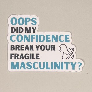 Könnte beinhalten: Ein weißer Aufkleber mit dem Text "OOPS DID MY CONFIDENCE BREAK YOUR FRAGILE MASCULINITY?" in Schwarz und Blaugrün. Eine Schnuller-Grafik befindet sich neben dem Text. Der Aufkleber hat einen weißen Rand und einen hellgrauen Hintergrund.