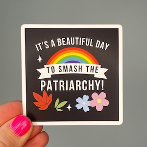 May include: Square sticker with a black background featuring the text "IT'S A BEAUTIFUL DAY TO SMASH THE PATRIARCHY!" above a rainbow and banner. The sticker also includes leaf and flower illustrations.