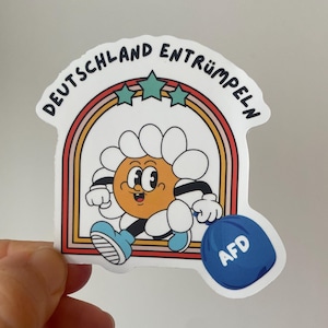 Może przedstawiać: Naklejka z uśmiechniętą stokrotką z kreskówek biegnącą w tęczowym łuku. Tekst "DEUTSCHLAND ENTRÜMPELN" jest wygięty nad stokrotką. Niebieski obiekt z napisem "AFD" znajduje się w prawym dolnym rogu.