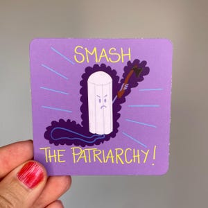 Könnte beinhalten: Ein quadratischer violetter Aufkleber mit einer animierten Tampon-Figur mit wütendem Gesichtsausdruck, die eine kleine braune Axt hält. Der Text SMASH THE PATRIARCHY ist in gelben Buchstaben um die Figur gedruckt, ergänzt durch hellblaue Linien.