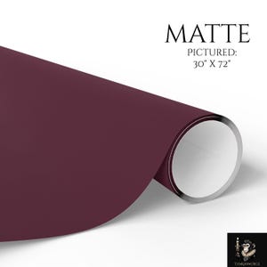 May include: A roll of matte finish dark burgundy paper with a smooth texture. The text MATTE PICTURED: 30" X 72" is printed in black above the roll. A small logo featuring a monkey holding a candle is visible in the bottom right corner.