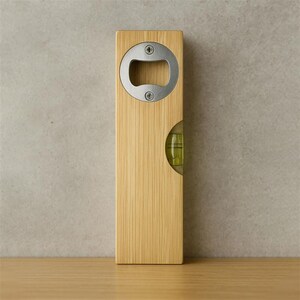 Op de afbeelding: Een houten flesopener met een ingebouwd waterpas. De opener heeft een roestvrijstalen flesopener en een kleine waterpas. Het hout heeft een lichtbruine kleur en een verticaal nerfpatroon.