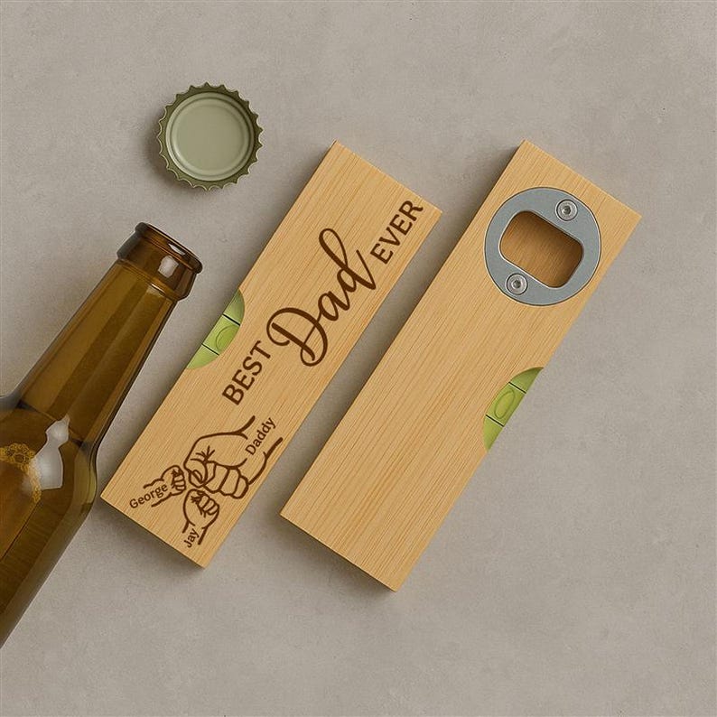 Op de afbeelding: Een houten flesopener met de tekst "Best Dad Ever", een waterpas en een flesdop. De opener heeft een metalen flesopener en een waterpasbel.
