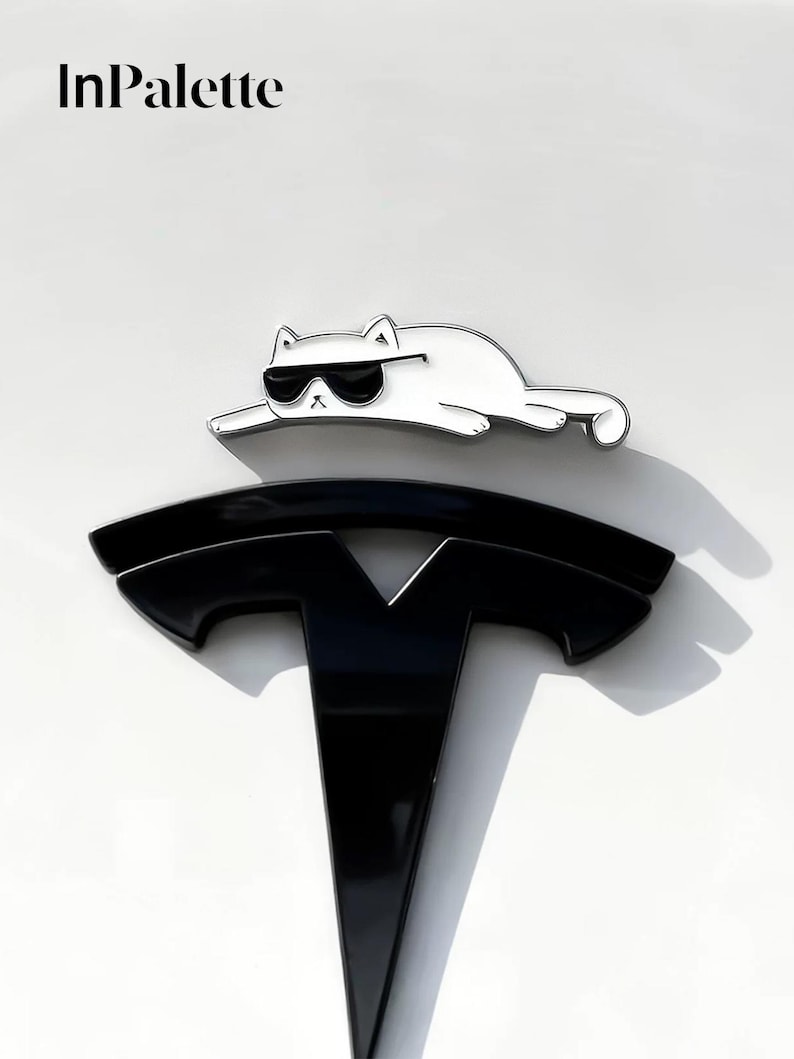 May include: A white cat wearing sunglasses is positioned above a black Tesla logo on a white surface. The text "InPalette" is in the upper left corner. The cat is a fun, decorative element.