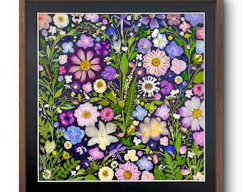 Può includere: Un'opera d'arte floreale incorniciata con una vivace disposizione di fiori pressati in vari colori, tra cui rosa, viola, bianco e giallo. I fiori sono disposti su uno sfondo scuro e incorniciati in una cornice di legno marrone.