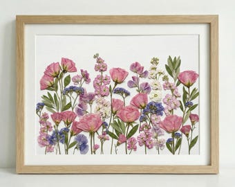 Può includere: Stampa floreale incorniciata con fiori pressati rosa, viola, blu e bianchi. I fiori sono disposti su uno sfondo bianco e incorniciati in una cornice di legno chiaro. L'opera d'arte ha un tema botanico.