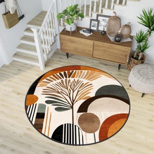 May include: A round, cream-coloured rug with a black border. The rug features a stylised tree with brown branches and green leaves, surrounded by geometric shapes in shades of brown, orange, and grey.
