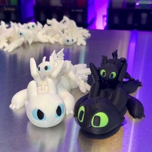 May include: A collection of dragon figurines in white and black. The white dragons have blue eyes, while the black dragons have green eyes. The figurines are on a reflective surface, with a purple background.