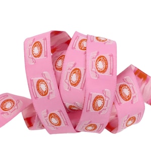 May include: Pink ribbon featuring a repeating pattern of orange rotary phones. The ribbon is curled and twisted, showcasing the phone design. The ribbon's edges have a subtle, textured appearance.