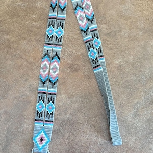 May include: A gray lanyard with a geometric pattern in blue, pink, black, and white. The lanyard has a silver-colored metal clasp. The design is repeated along the length of the lanyard.
